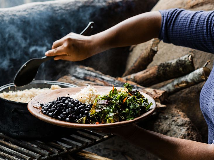 A woman out of frame puts a scoop of rice on a plate full of navy beans and salad