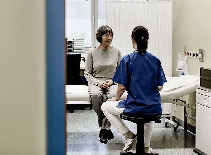 doctor in blue scrubs faces older patient sitting on hospital bed