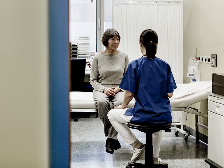 doctor in blue scrubs faces older patient sitting on hospital bed