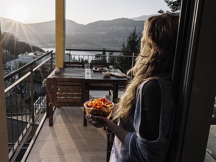 A woman holds a bowl of vegetables while looking at the scenery from a terrace
