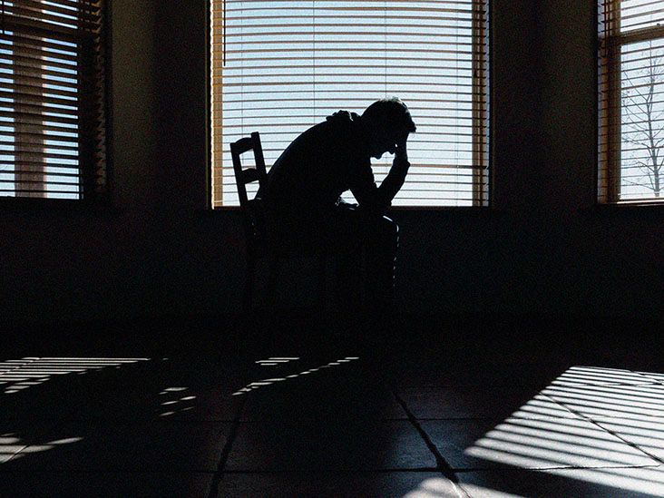A man holds his head in his hands as he sits on a bed