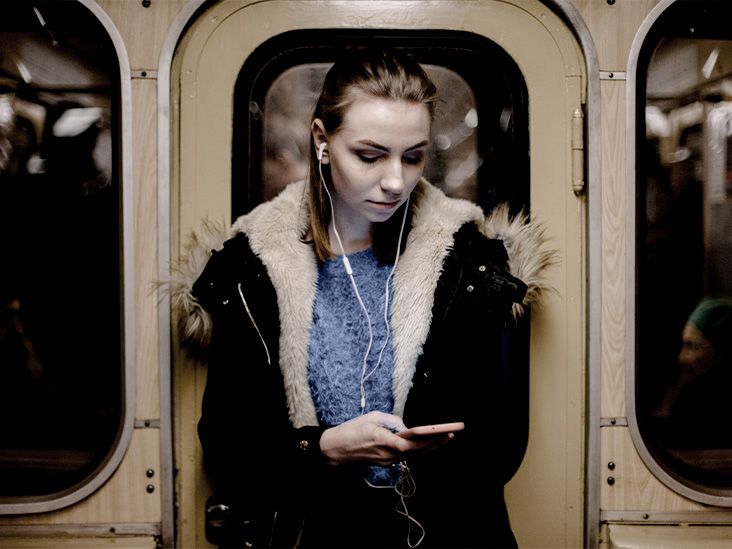 A woman standing in a subway car listens to music on her iPhone