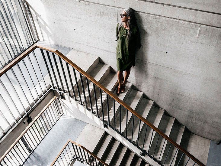 A woman with long gray hair leaning against a wall in a staircase