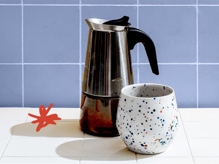 metal coffee pitcher and white cup with colorful speckles against a blue tile background