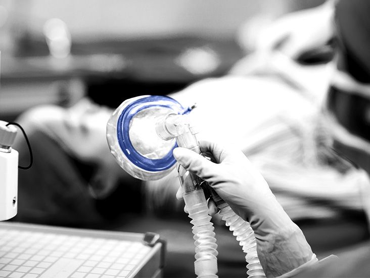 A nurse prepares to put an oxygen mask on a person undergoing surgery