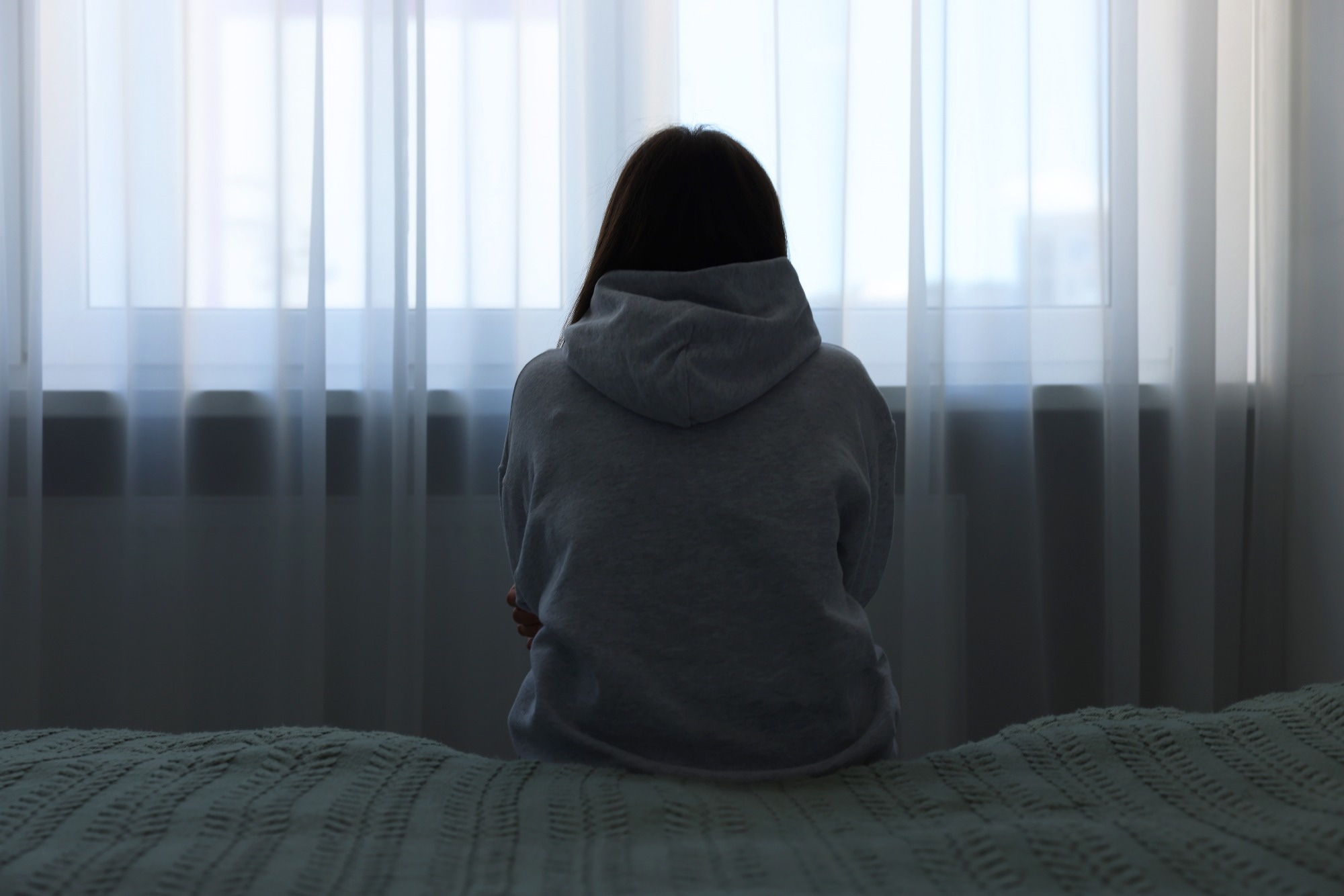 Sad woman sitting on bed at home.