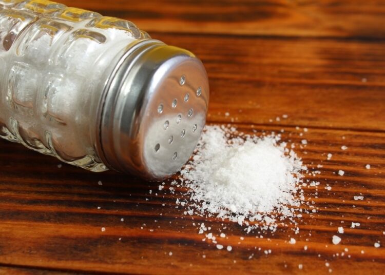 On a wooden table lies a glass salt shaker with overturned salt.