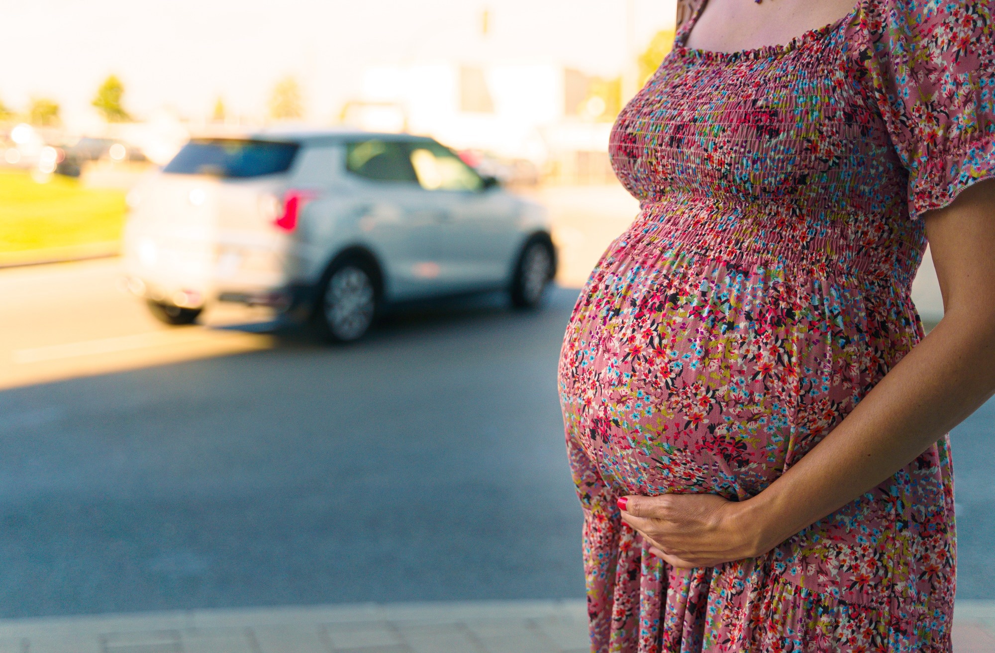 Close-up of a pregnant belly with a city street on the background.