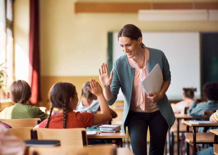 Happy elementary school teacher giving high-five to her student during class in the classroom.
