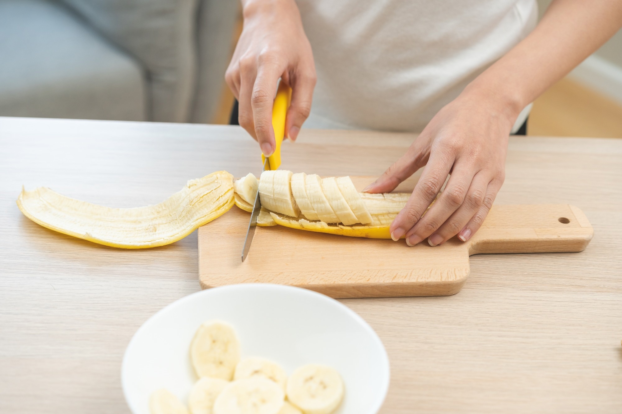 woman cutting banana slices on table.