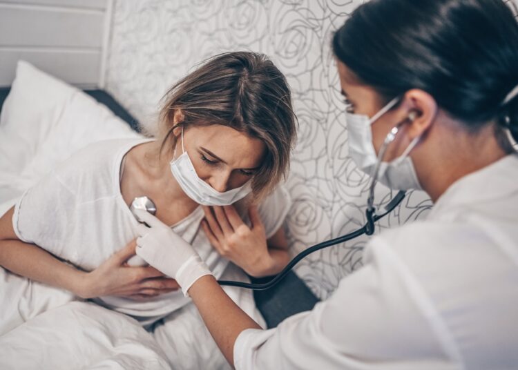 Doctor nurse in protective face mask listening to breath with a stethoscope suspecting Coronavirus (COVID-19)