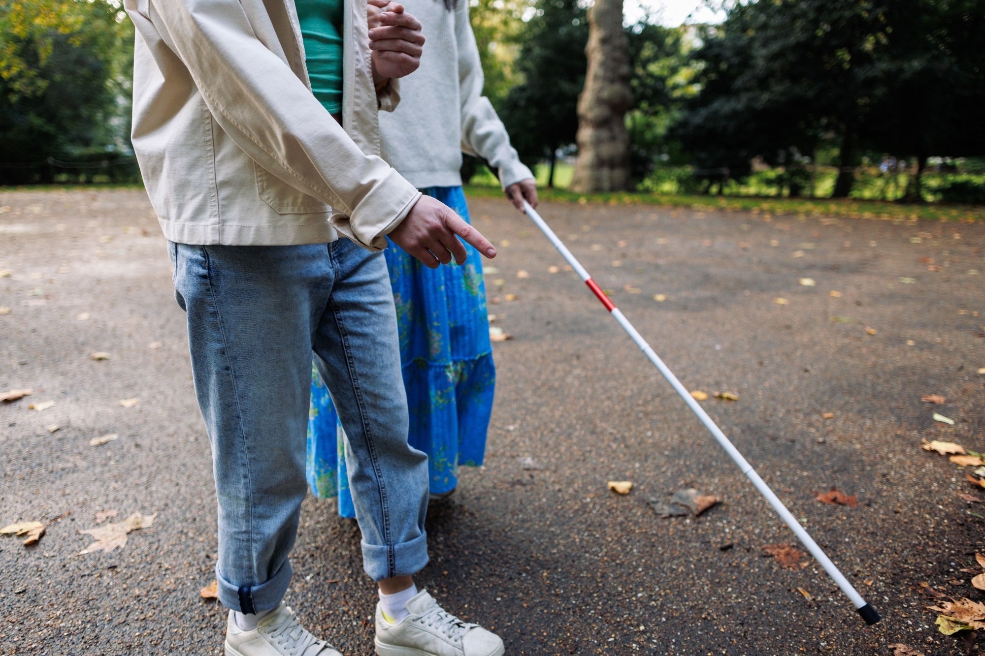 Visually impaired woman with white cane in park being guided by young man