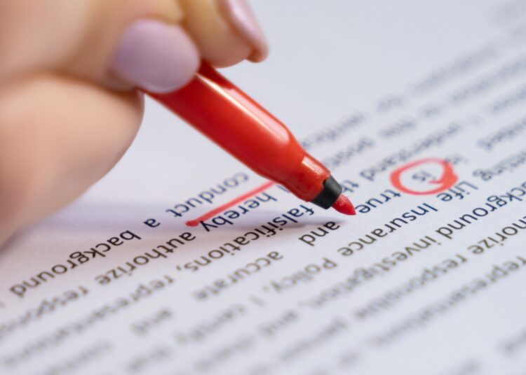 A person uses a red pen to mark and correct text on a printed document.