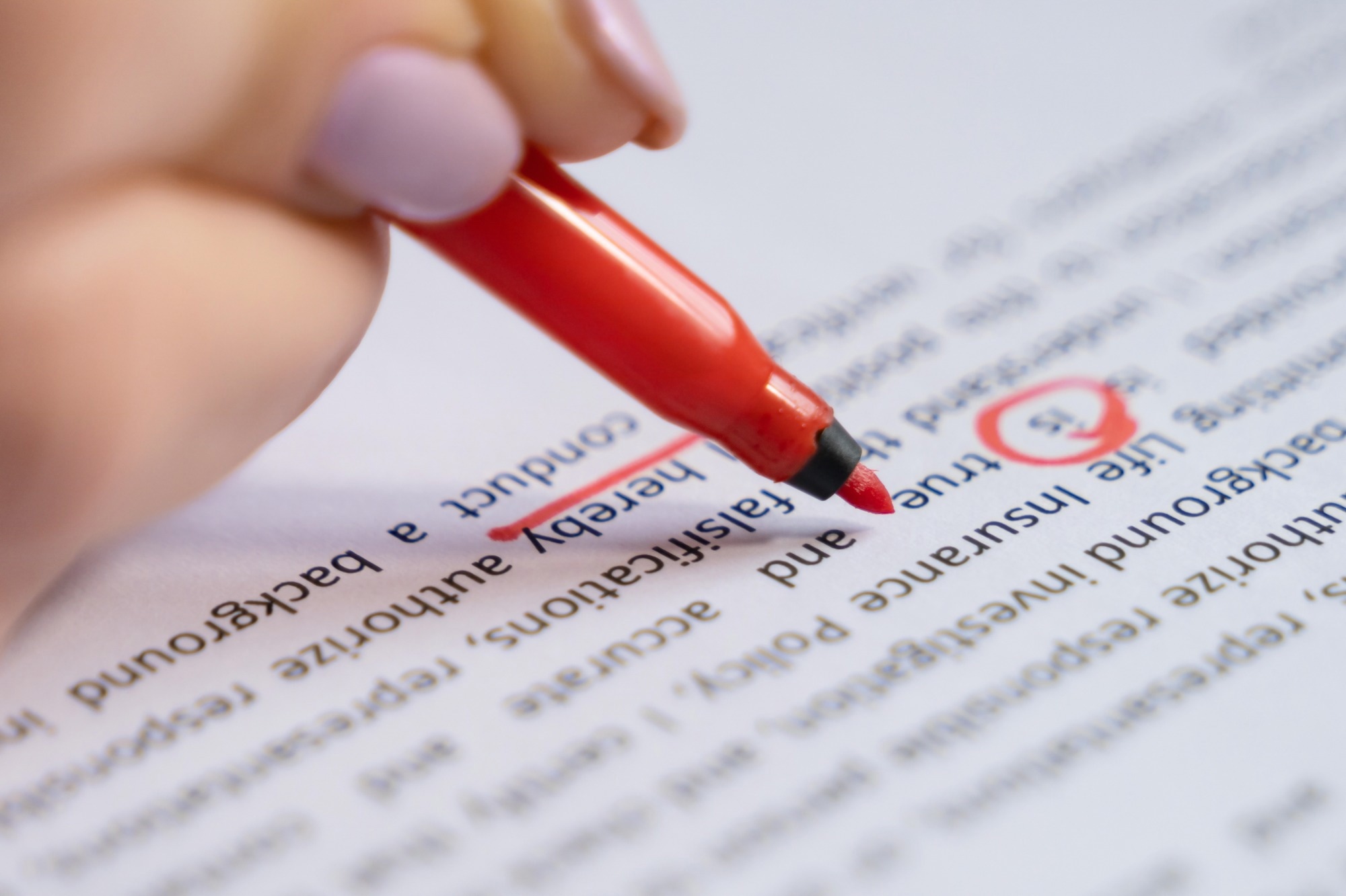 A person uses a red pen to mark and correct text on a printed document.