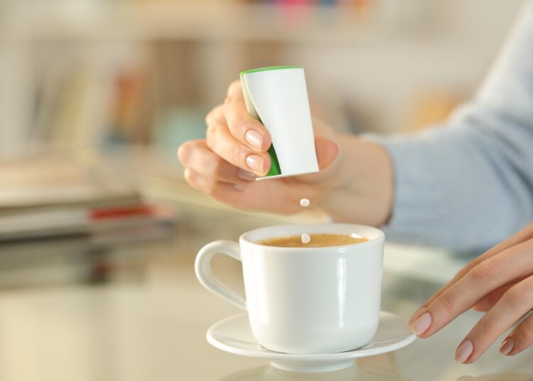 Close up of woman hand throwing sweetner pills on coffee cup on a desk at home