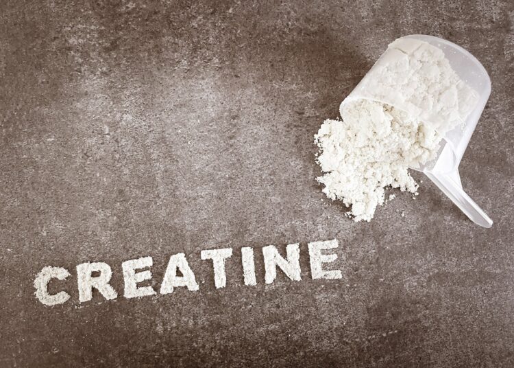 Creatine powder text font on grey stone background with plastic spoon cup