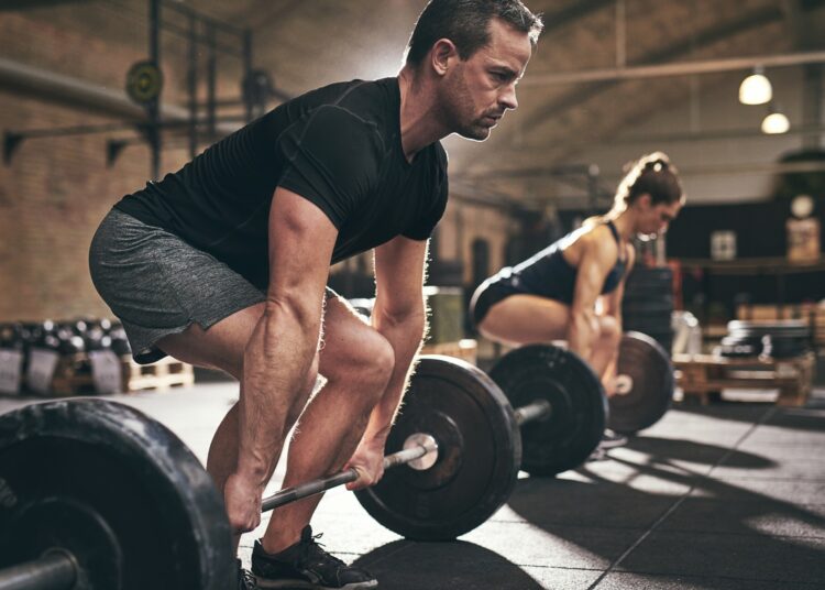Sporty man and woman are about to lift barbells in gym
