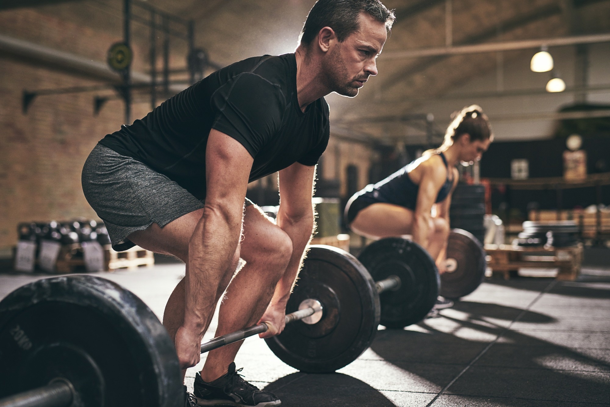 Sporty man and woman are about to lift barbells in gym