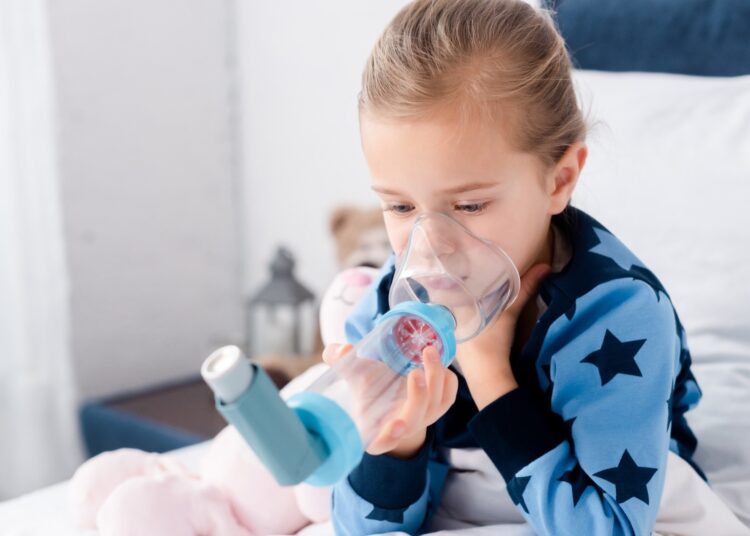 sick child using inhaler with spacer in bedroom
