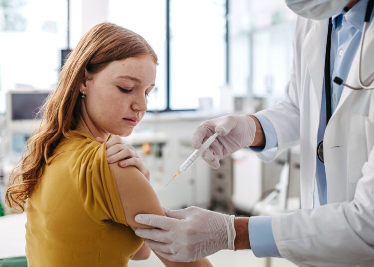 pediatrician injecting vaccine into teenage girl arm