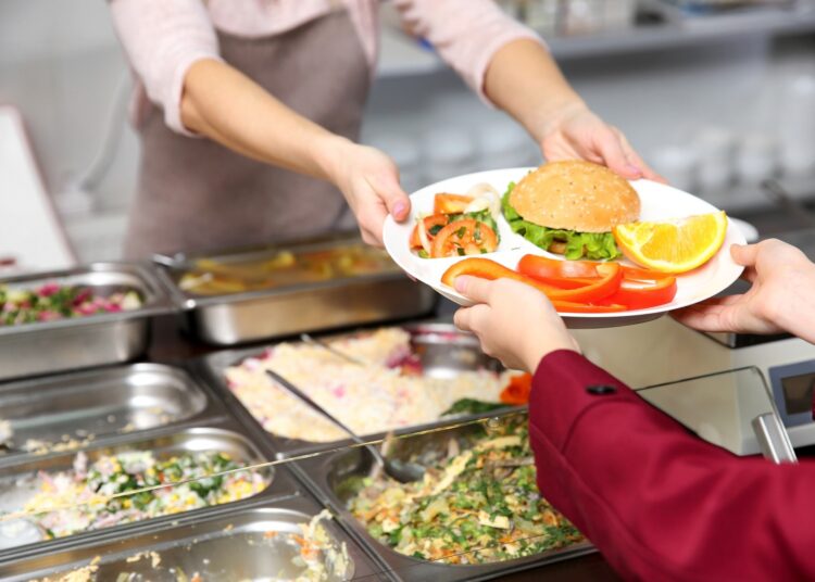 Pleasant woman giving lunch to school girl in cafeteria