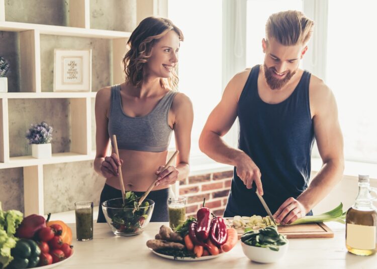 young sports people are talking and smiling while cooking healthy food in kitchen at home
