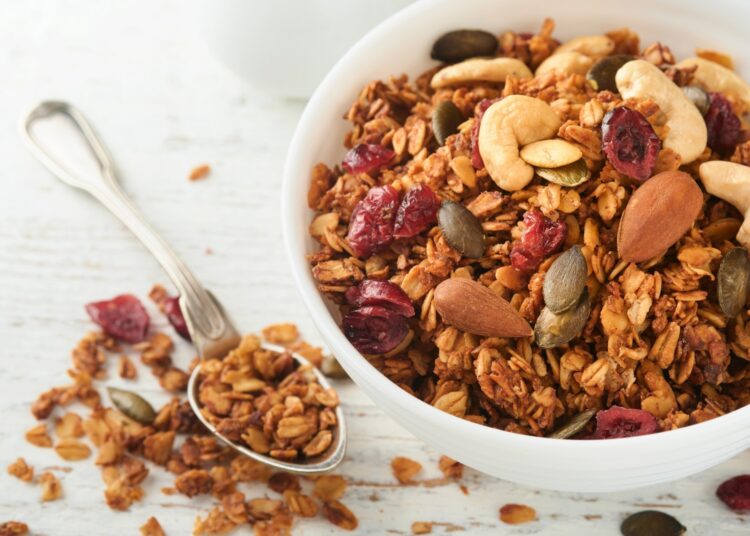 Homemade granola in glass jar with greek yogurt or milk and cashews, almonds, pumpkin with dried cranberry seeds