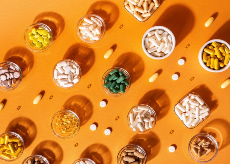Organic dietary supplements, many capsules of vitamins and minerals in small bowls from above on an orange background.