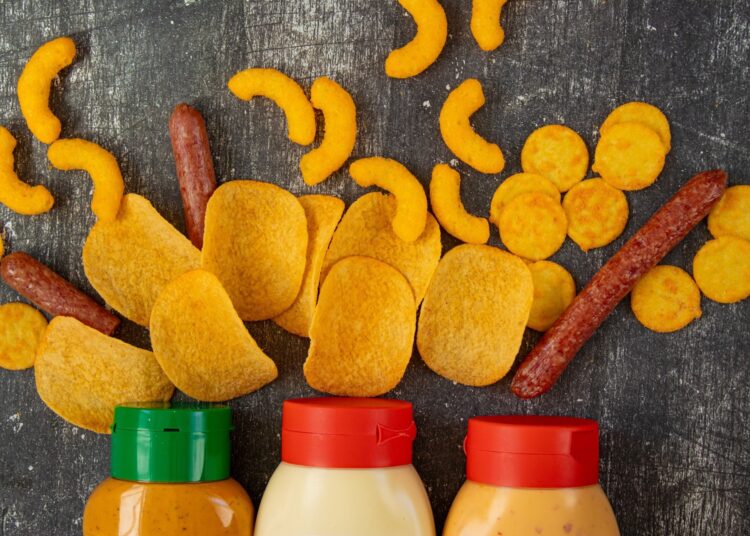 Fast food, unhealthy snacks, chips, sausages, and harmful sauces on a black background.