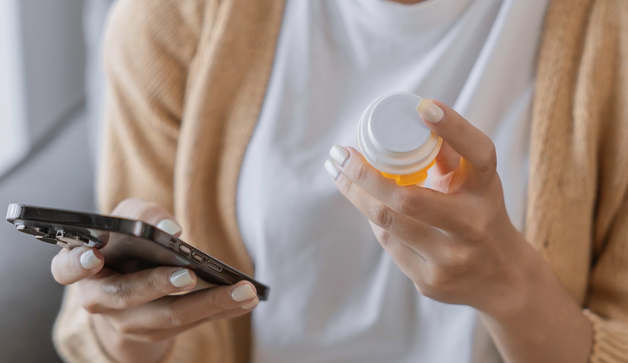 Woman reading information online on mobile phone holding bottled prescription drug