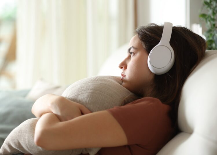 Sad and melancholic woman listening music with headphone at home
