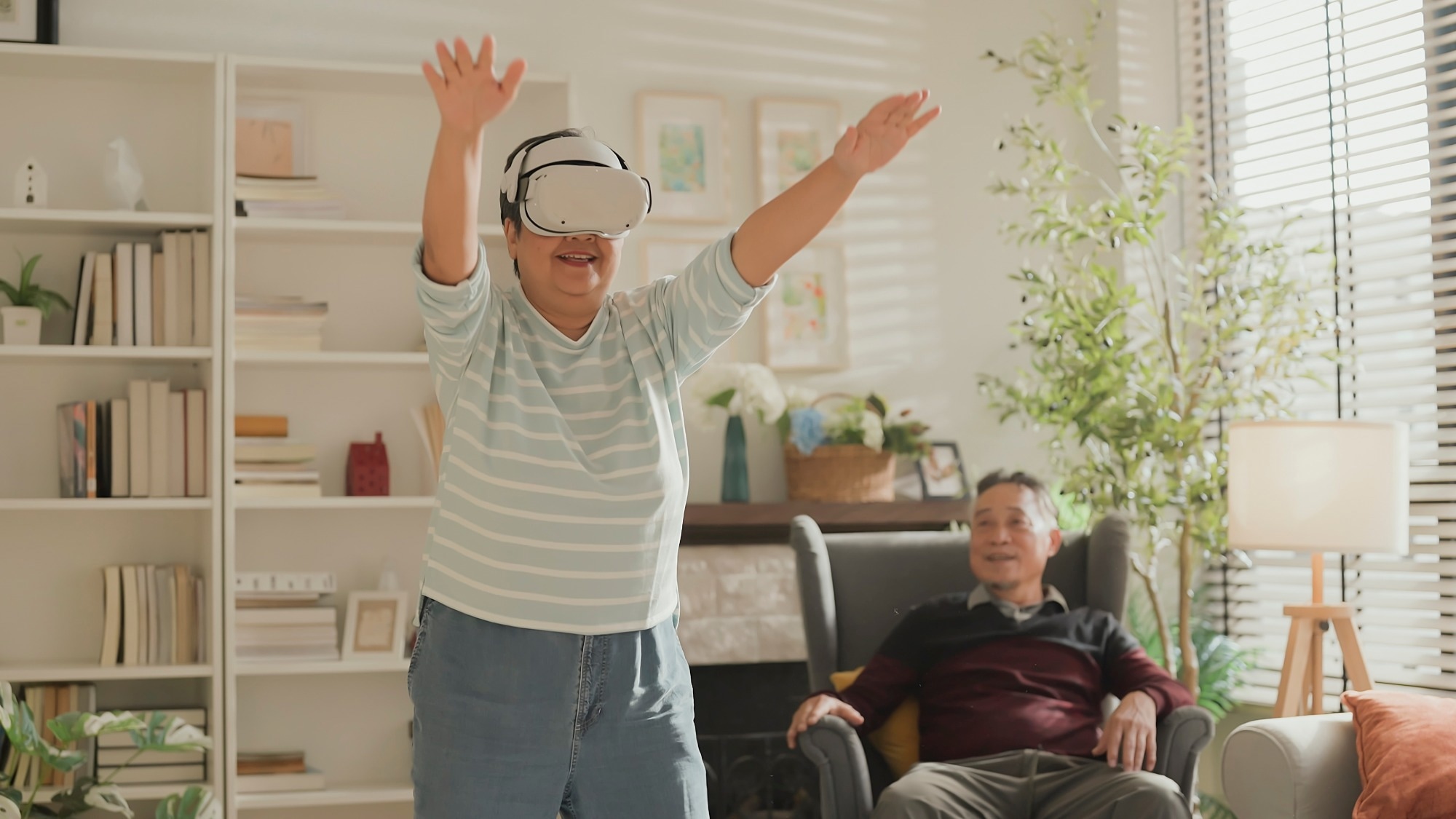 Older adult couple in living room. Woman using VR experience to do gentle exercise movement