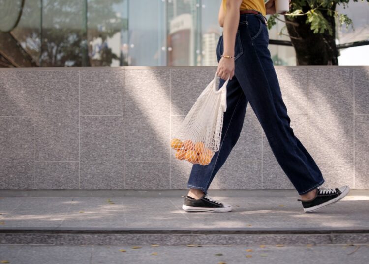 young woman walking carrying a shopping bag of oranges