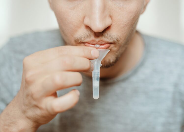 man spitting with mouth through funnel in plastic tube to collect sample