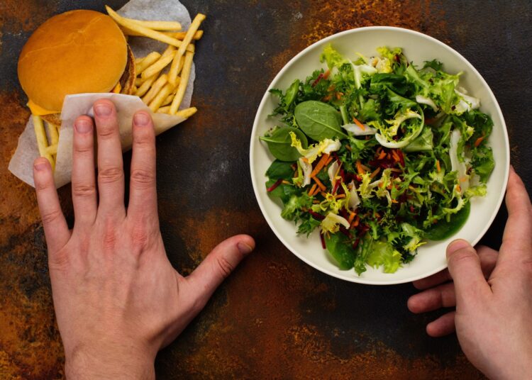 Young man making choice between salad and fast food