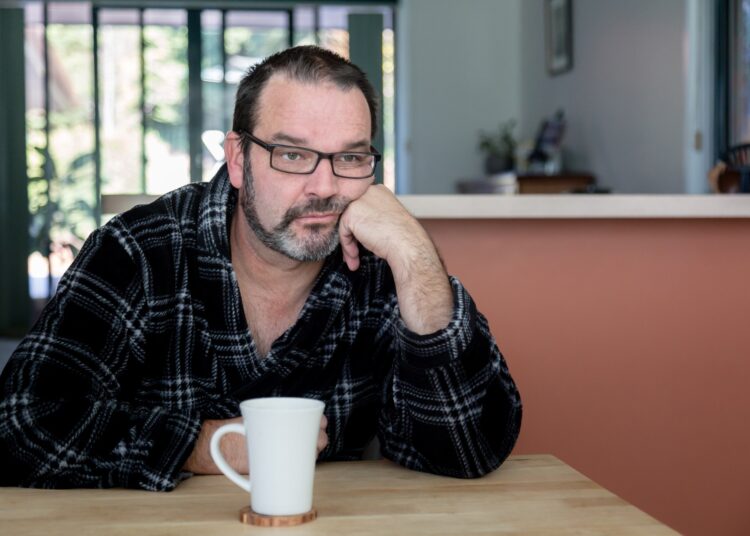 Middle aged man sitting at dining room table with coffee mug looking sad and depressed