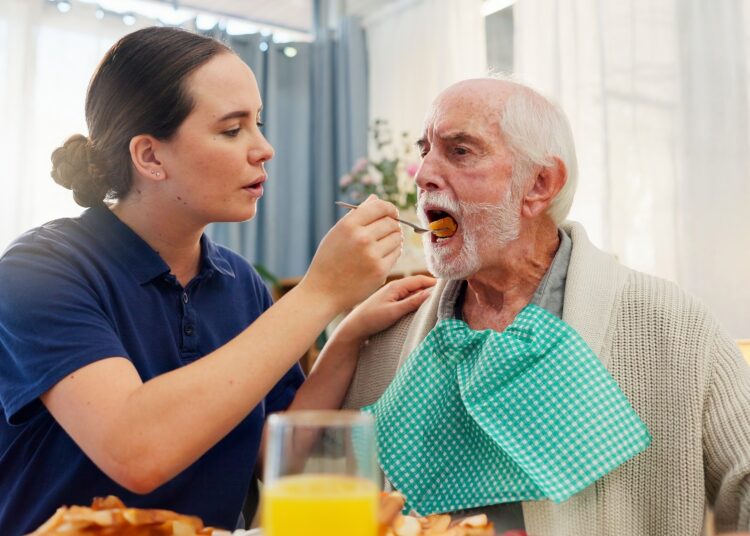 Female healthcare work feeding an elderly male patient with a spoon