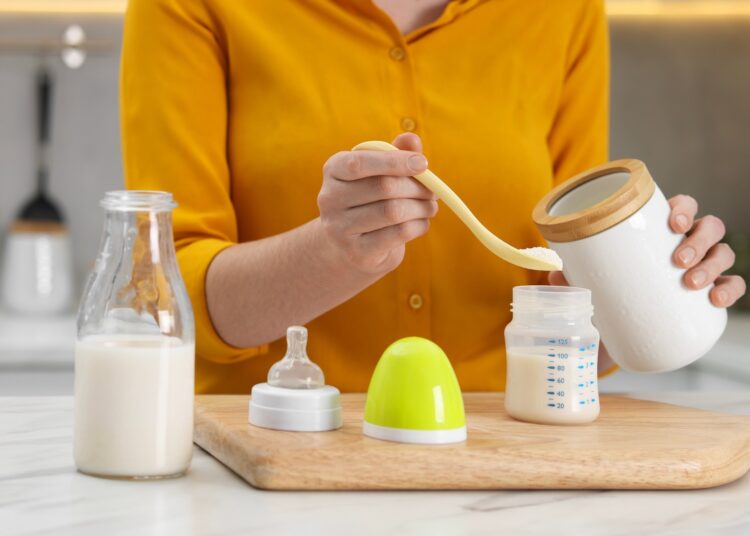 Mother making baby formula in feeding bottle at table