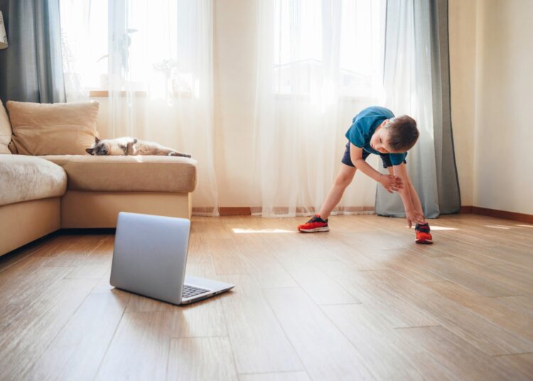 The boy doing physical exercises, watching video lesson online in front of open laptop computer