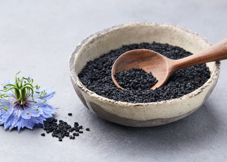 Black cumin seeds with nigella sativa flower on grey background