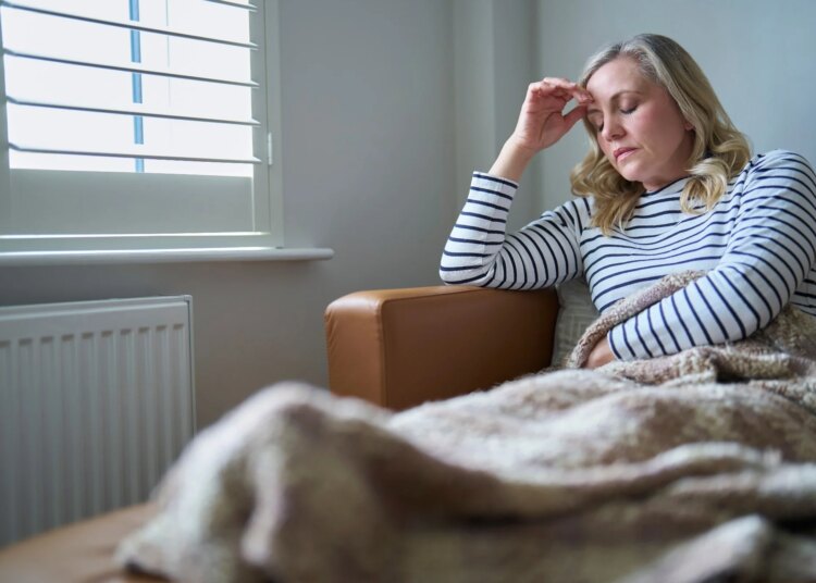 Mature Woman Suffering With Long Term Illness Sitting On Sofa At Home