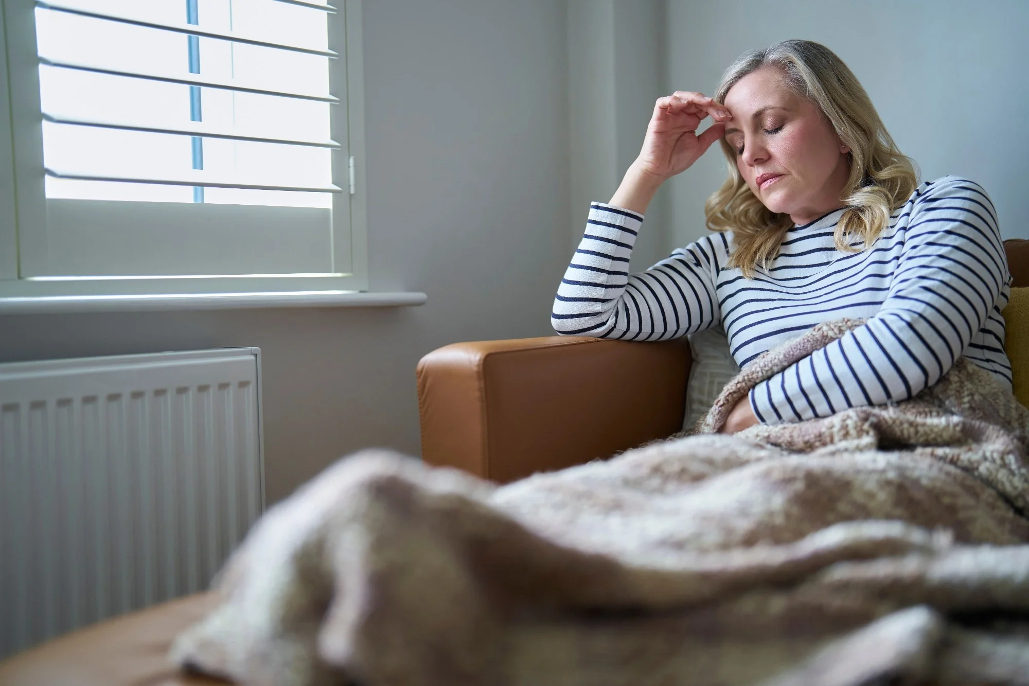 Mature Woman Suffering With Long Term Illness Sitting On Sofa At Home