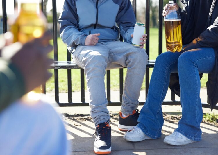 Close Up Of Underage Teenagers Drinking Alcohol In Park
