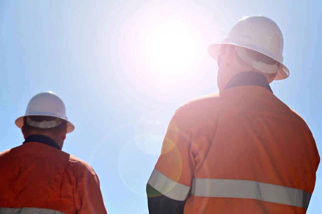 Two unrecognizable blue collar workers isolated against clear blue sky with sun flare.
