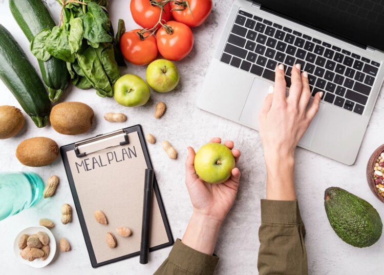 Woman workspace with healthy food. Female hands writing in the notepad words