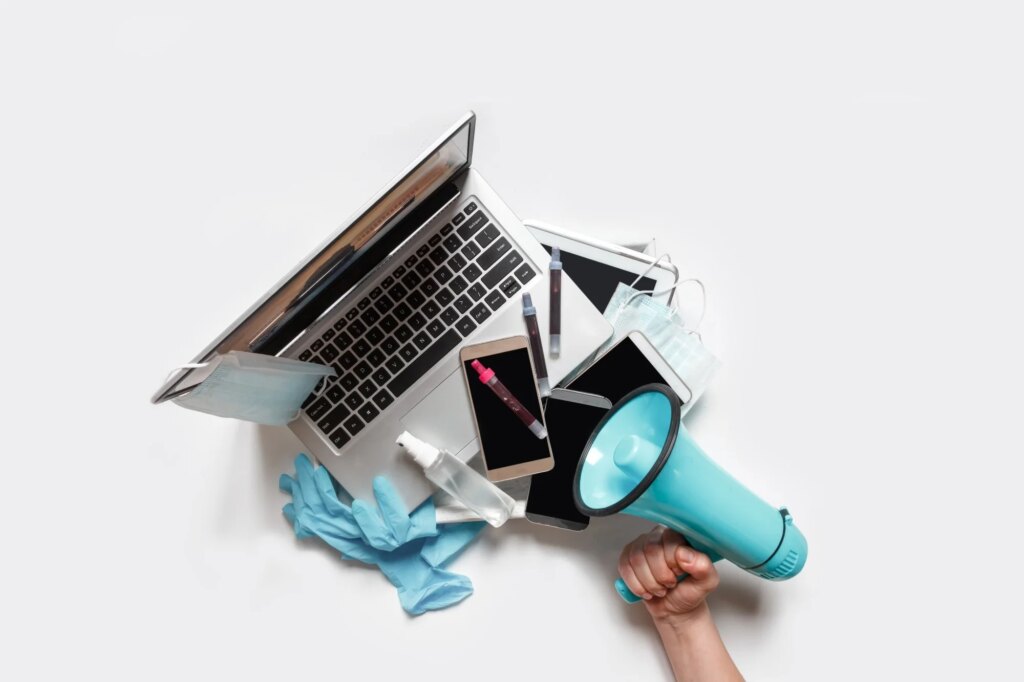 Hands holding a tray with digital gadgets. Laptop. Phone from which they broadcast information. Hand with megaphone to the right