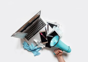 Hands holding a tray with digital gadgets. Laptop. Phone from which they broadcast information. Hand with megaphone to the right