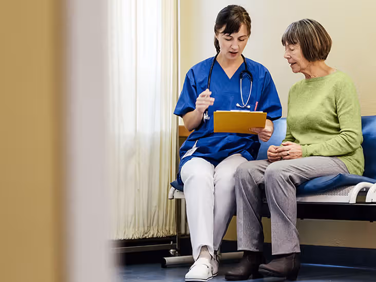 A healthcare professional talks with an older adult patient with a clipboard in hand