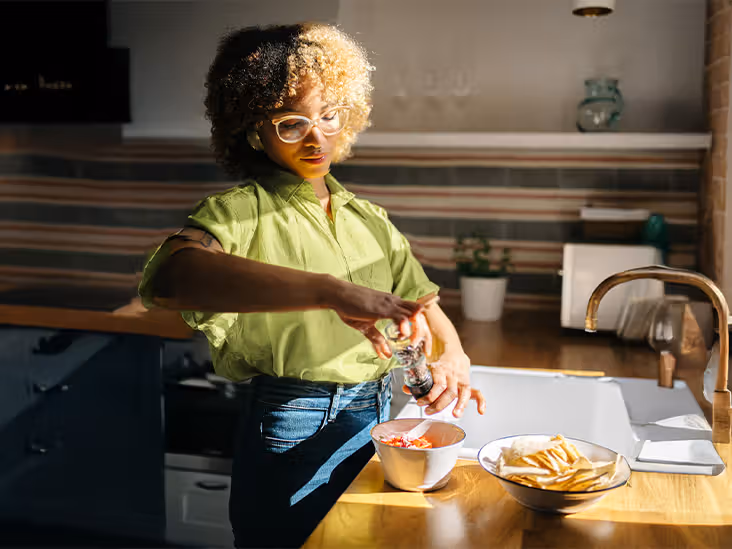 A person prepares a bowl of food, grinding pepper over it next to a bowl of tortilla chips