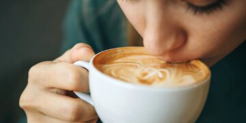 Close up girl is drinking coffee. She enjoys her morning cappuccino or flat white.
